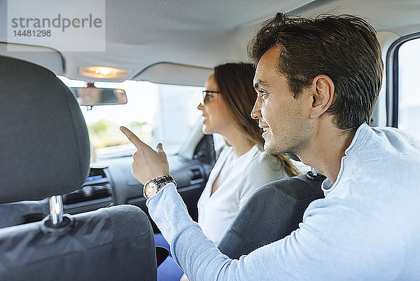 Ehepaar im Auto mit Frau auf dem Beifahrersitz und Mann  der vom Rücksitz aus mit dem Finger zeigt