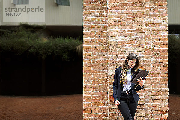Junge Geschäftsfrau steht mit Tablette an Backsteinsäule
