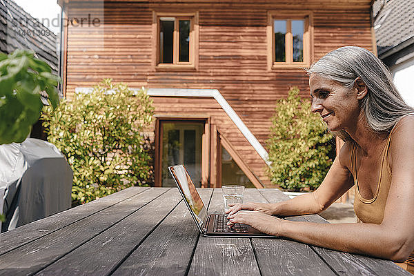 Frau sitzt mit Laptop auf der Terrasse ihres Hauses