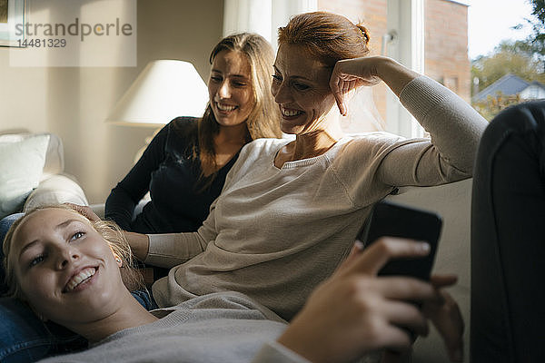 Glückliche Mutter mit zwei Teenager-Mädchen auf der Couch zu Hause mit Handy