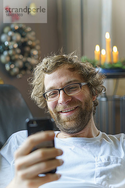 Porträt eines glücklichen Mannes mit Smartphone zur Weihnachtszeit zu Hause