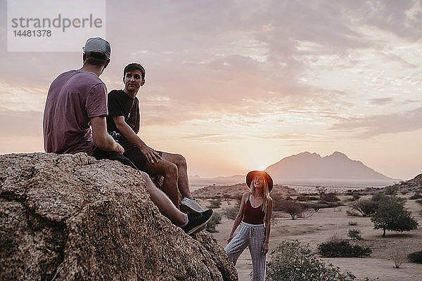 Namibia  Spitzkoppe  Freunde sitzen bei Sonnenuntergang auf einem Felsen