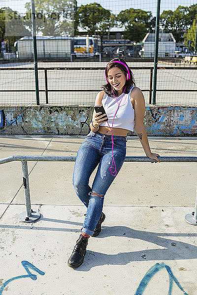 Lächelnde junge Frau mit Kopfhörer und Handy in der Stadt