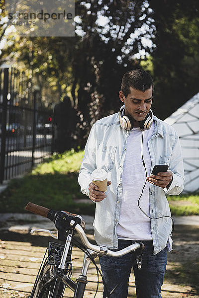 Junger Mann mit Fahrrad und Kaffee zum Mitnehmen prüft Handy