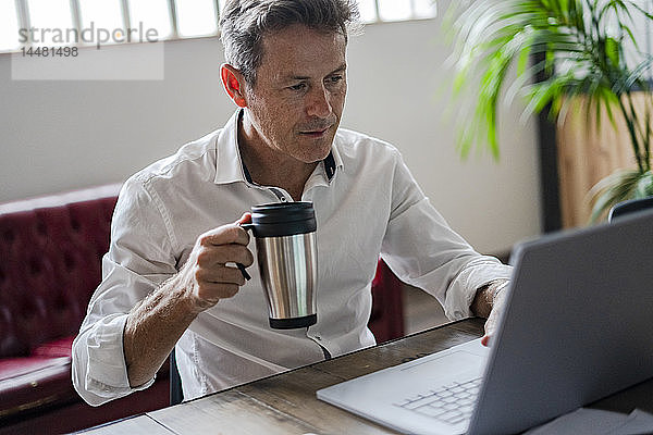 Geschäftsmann hält Kaffeetasse mit Laptop am Schreibtisch