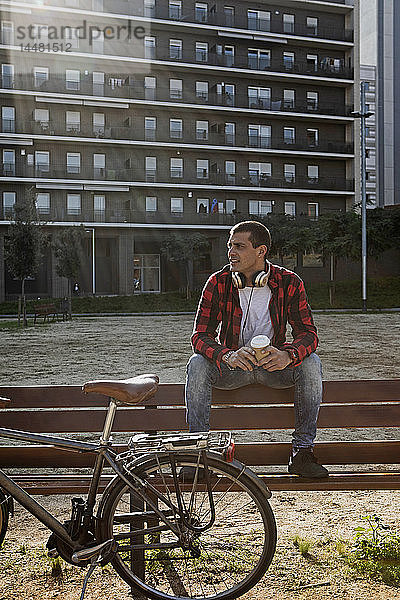 Junger Mann sitzt auf einer Bank in der Stadt neben dem Fahrrad
