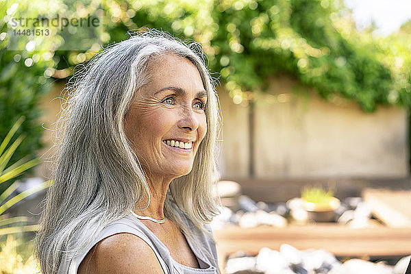 Bildnis einer lächelnden Frau mit langen grauen Haaren im Garten