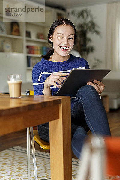 Junge Frau sitzt zu Hause und benutzt ein digitales Tablett
