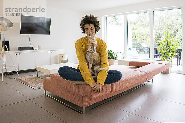 Frau mit Hund sitzt zu Hause auf dem Sofa