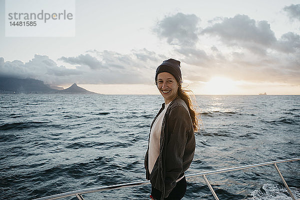Südafrika  junge Frau mit Wollmütze lächelt während einer Bootsfahrt bei Sonnenuntergang