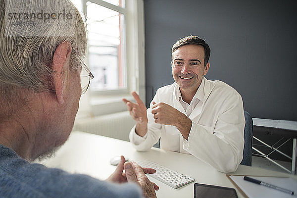 Lächelnder Arzt im Gespräch mit Patient in der medizinischen Praxis