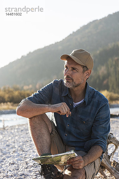 Erwachsener Mann zeltet am Flussufer  sitzt auf Baumstamm mit Karte