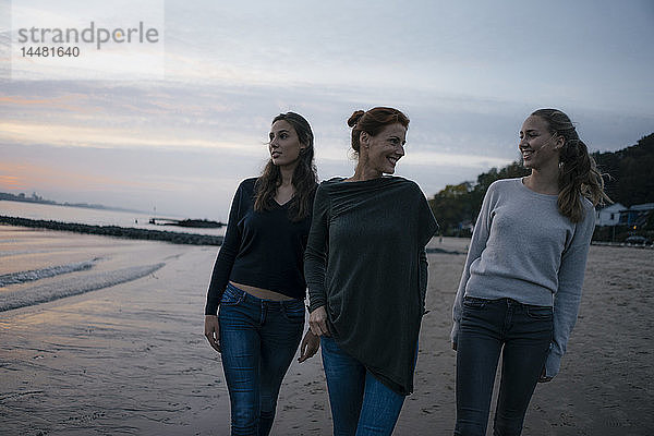 Deutschland  Hamburg  glückliche Mutter mit zwei Teenager-Mädchen  die abends am Strand am Elbufer spazieren gehen