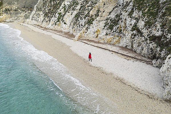 Italien  Elba  Frau mit rotem Mantel beim Strandspaziergang  Luftaufnahme mit Drohne