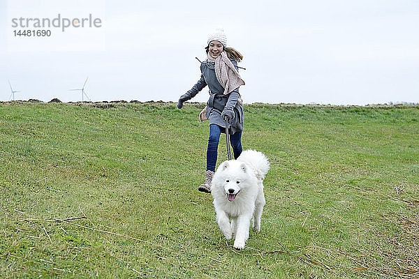 Lachendes Mädchen rennt mit ihrem Hund auf einer Wiese