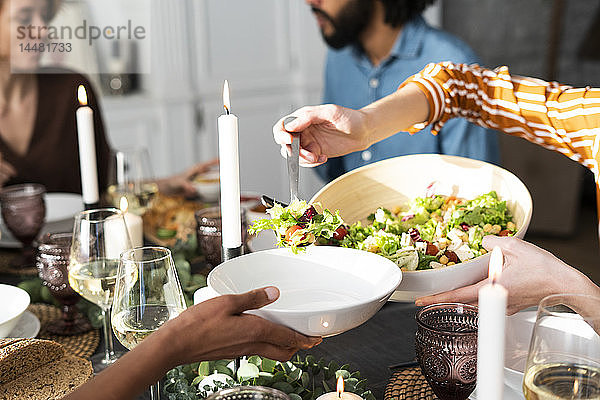 Frau serviert Salat auf dem Teller eines Freundes bei einer Dinnerparty