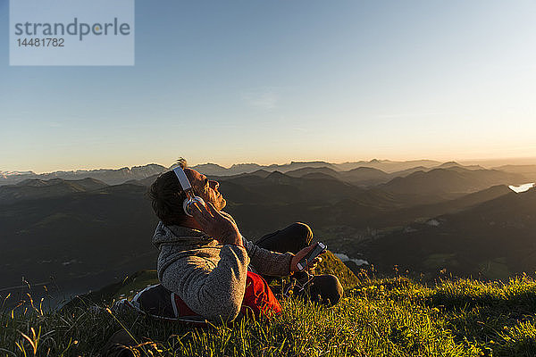 Wanderer  der im Gras liegt  eine Pause macht und mit Kopfhörern Musik hört