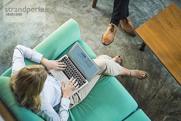 Draufsicht einer Geschäftsfrau  die am Laptop auf einer türkisfarbenen Couch im Coworking Space arbeitet