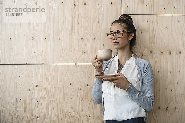Junge Frau  die im Kreativbüro arbeitet  eine Pause macht und Kaffee aus einer Holztasse trinkt