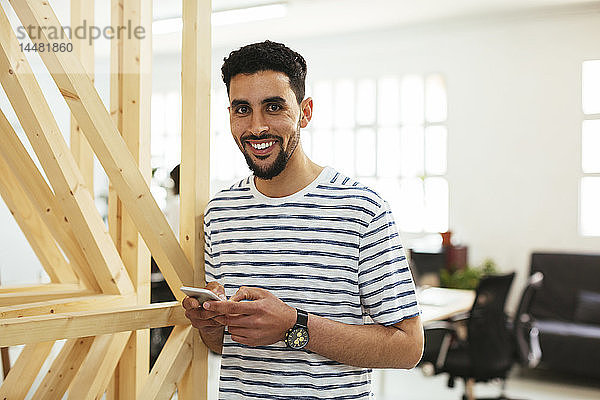 Porträt eines lächelnden jungen Mannes mit Handy im Büro