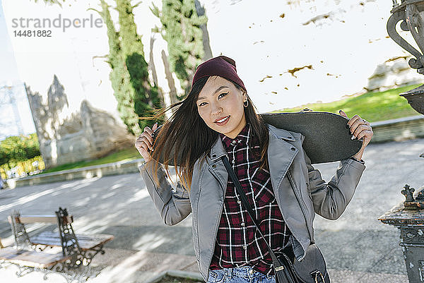 Porträt einer lächelnden jungen Frau mit Skateboard auf den Schultern