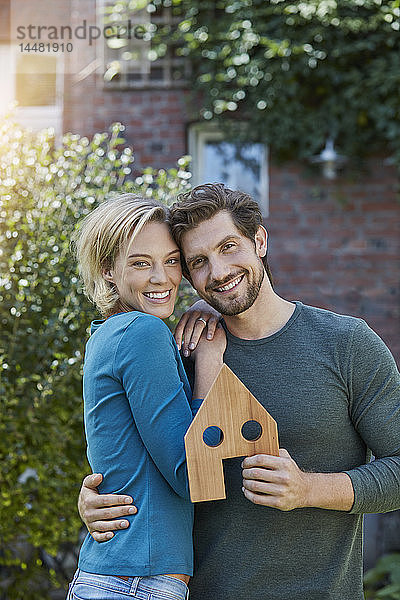 Porträt eines glücklichen Paares vor ihrem Haus mit Hausmodell