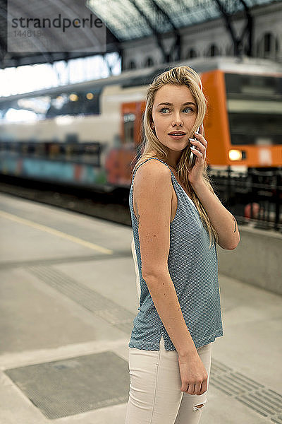 Junge Frau am Bahnhof am Handy  die sich umsieht