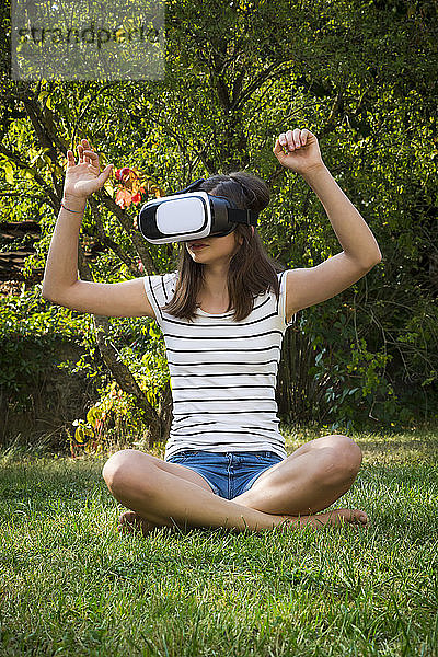 Mädchen sitzt auf der Wiese im Garten und benutzt eine Virtual-Reality-Brille