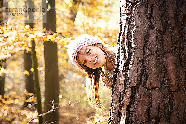 Junges Mädchen hinter Baum im Herbst