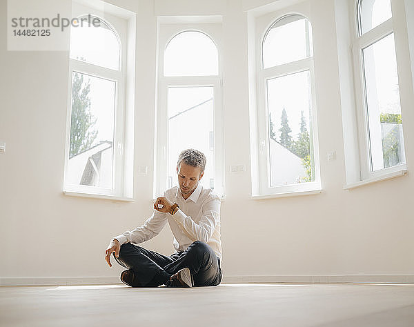Geschäftsmann sitzt auf dem Boden seines frisch renovierten Hauses und prüft die Zeit