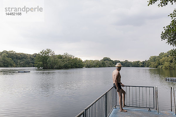 Älterer Mann mit Strohhut steht an einem See