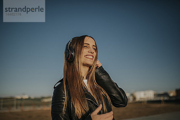 Glückliche junge Frau  die im Freien mit Kopfhörern Musik hört