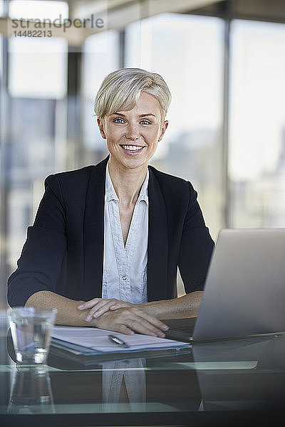 Porträt einer lächelnden Geschäftsfrau  die mit Laptop am Schreibtisch im Büro sitzt