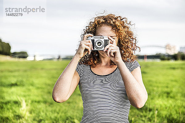 Junge Frau auf einer Wiese  die einen Betrachter mit der Kamera fotografiert