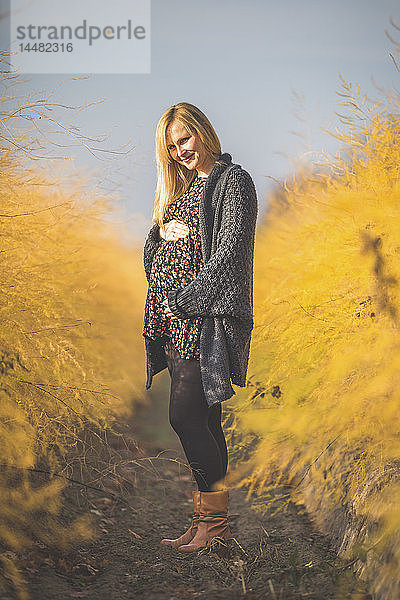 Lächelnde schwangere Frau steht im Herbst im Spargelfeld