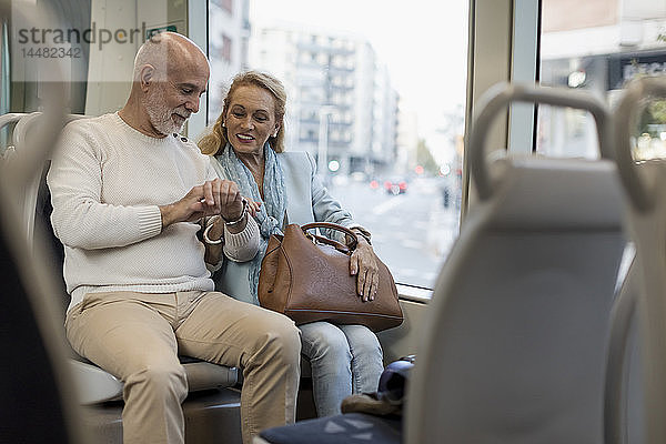 Älteres Ehepaar sitzt in einer Straßenbahn und kontrolliert die Zeit