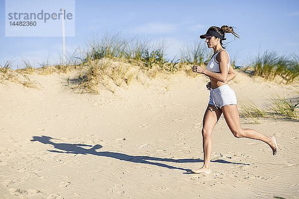 Sportliche Frau läuft am Strand entlang der Sanddünen