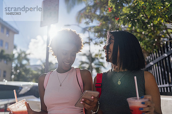 USA  Florida  Miami Beach  zwei glückliche Freundinnen mit Handy und Erfrischungsgetränk in der Stadt