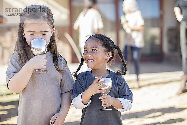 Porträt von zwei glücklichen Mädchen  die aus Kelche trinken