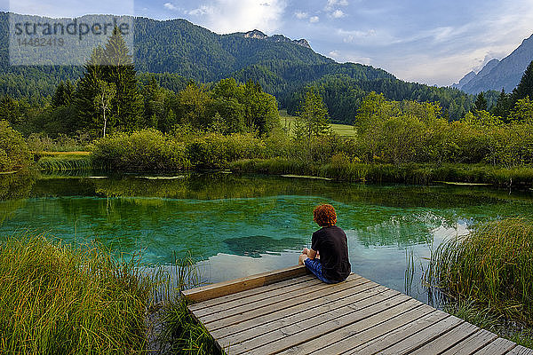 Slowenien  Gorenjska  bei Ratece  Sava Dolinka  Quelle  Zelenci-See  junger Mann am Steg sitzend