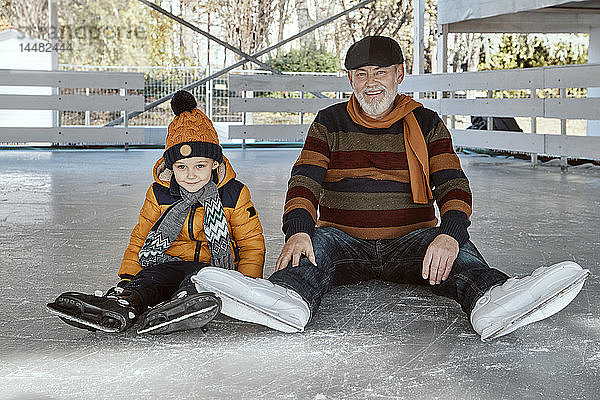 Grossvater und Enkel auf der Eisbahn  auf dem Eis sitzend