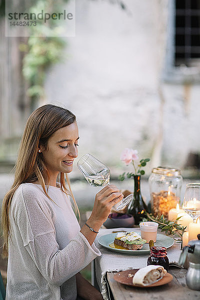 Frau probiert ein Glas Wein am Gartentisch