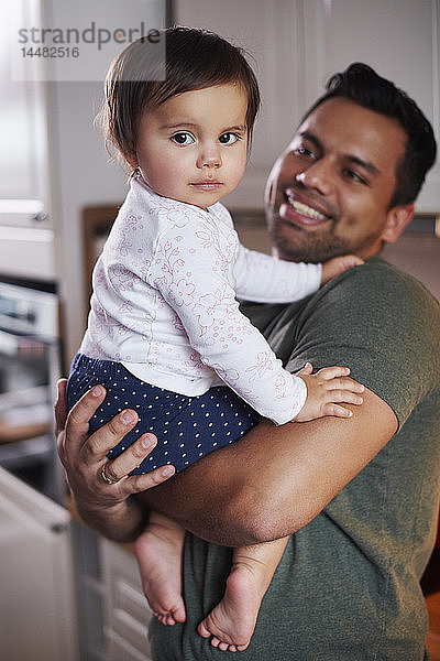 Porträt eines lächelnden Vaters  der ein kleines Mädchen zu Hause hält