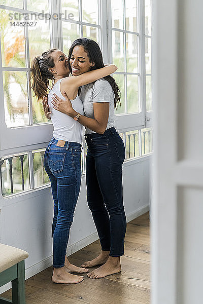 Zwei glückliche Freundinnen umarmen sich zu Hause am Fenster