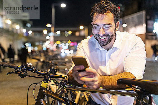 UK  London  glücklicher Mann  der nachts auf sein Telefon schaut