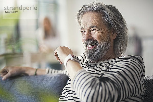 Älterer Mann sitzt auf der Couch und redet mit der Smartwatch