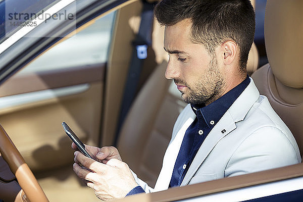 Junger Geschäftsmann sitzt im Auto und benutzt ein Smartphone