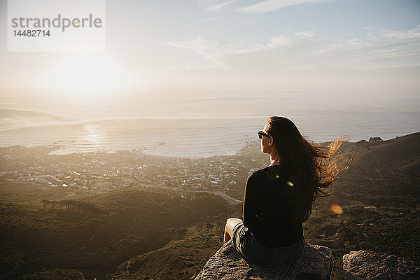 Südafrika  Kapstadt  Kloof Nek  Frau sitzt bei Sonnenuntergang auf einem Felsen