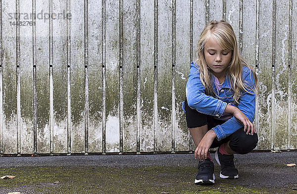 Porträt eines ernsten blonden Mädchens  das vor einer Holzwand kauert