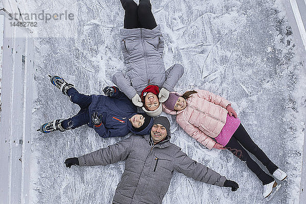 Familie mit zwei Kindern auf der Eisbahn  auf dem Eis liegend
